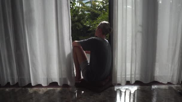 Мужчина смотрит на сад, сидя в панорамном французском окне — стоковое видео