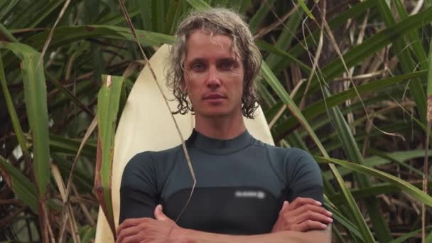 Surfista está bajo la palmera con los brazos cruzados en el pecho — Vídeo de stock
