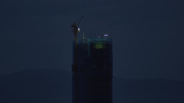 Tower kran nära hög hotellbyggnad silhuett på natten — Stockvideo