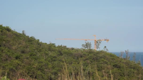 Grúa torre amarilla detrás de colina verde en la costa del mar en el complejo — Vídeo de stock