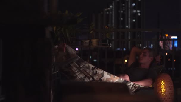 Homem adormecido encontra-se em rede multicolorida no terraço aberto — Vídeo de Stock