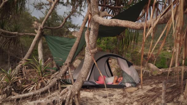 Dziewczyna śpi w namiocie na dzikiej plaży pod palmami — Wideo stockowe