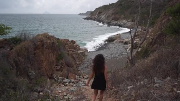 Donna con i capelli sciolti in abito nero cammina verso la spiaggia dell'oceano — Video Stock