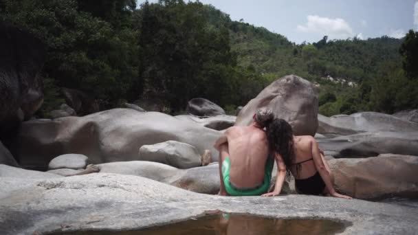 Kadın ve erkek, akıntılı düz kayalarda oturur manzaraya bakarlar. — Stok video