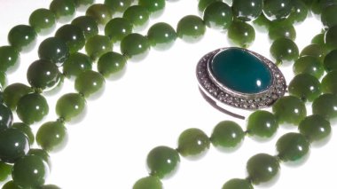 Beyaz arka planda yeşil mücevher. El yapımı ıvır zıvırları çevreleyen kolye boncukları. Süslerin, natürmortta birden fazla yeşil tonu vardır..