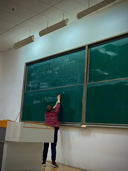 young woman in school uniform with backpack and books on the background of the blackboard