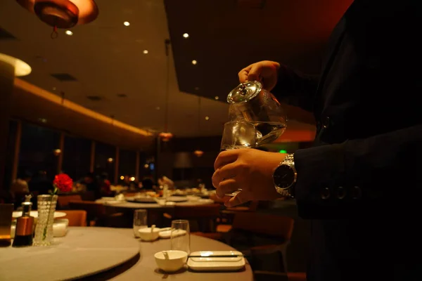 man pouring cocktail in a glass with a candle in the background