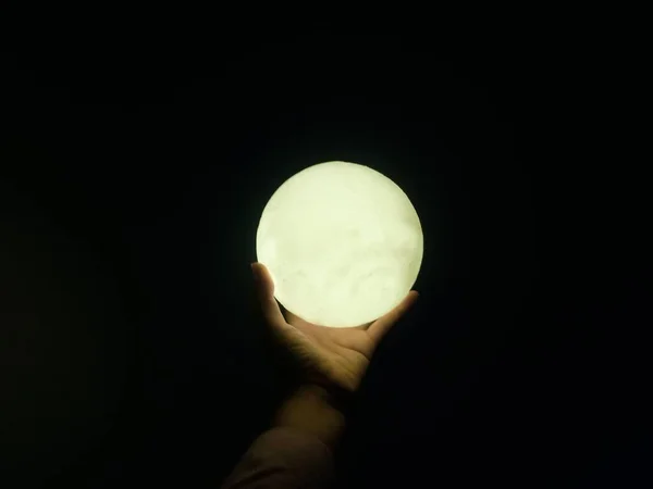 hand holding a white moon in the night sky