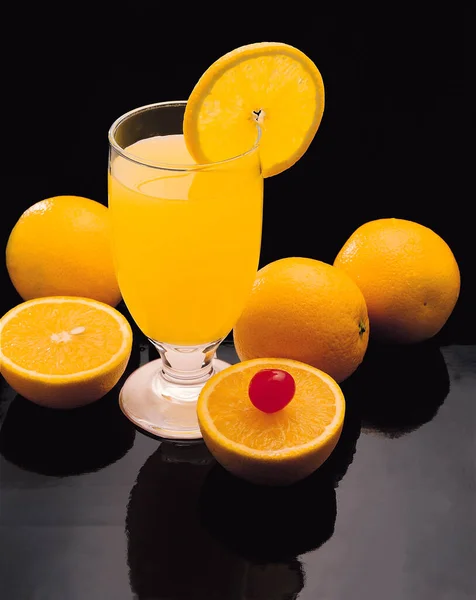 glass of orange juice and oranges on black background