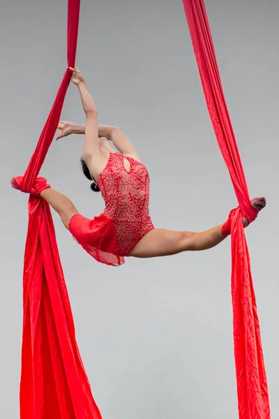 young woman gymnast performs acrobatic red rope on a pole.