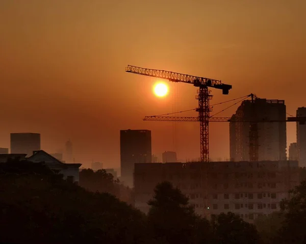 silhouette of a building with a crane and a city at sunset