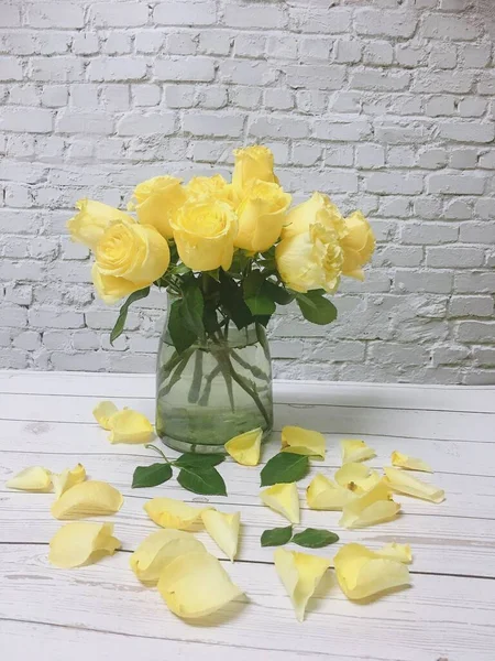 beautiful yellow roses in a vase on a white wooden background