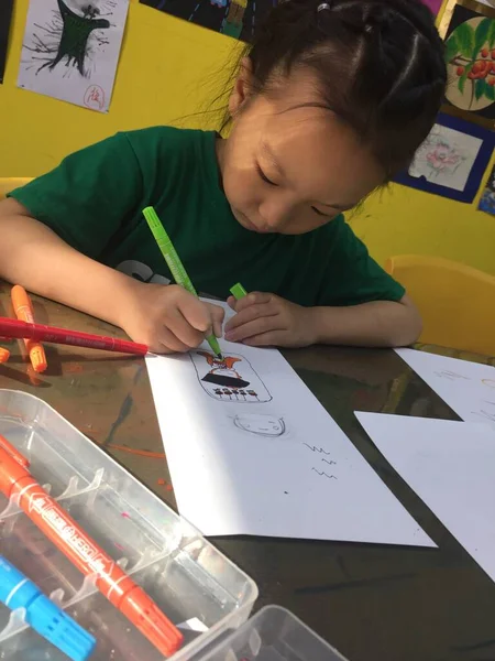 little girl draws a paper with a pencil on the table