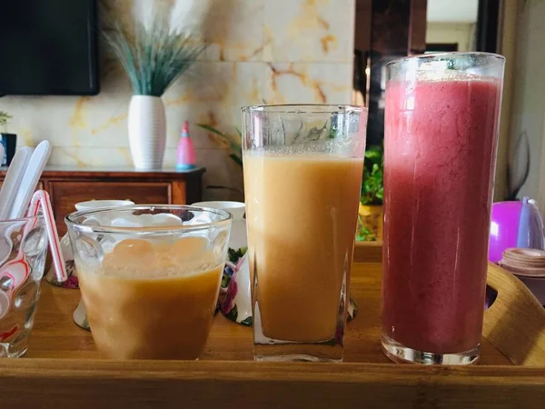a glass of fresh juice and a drink with a straw on a wooden table