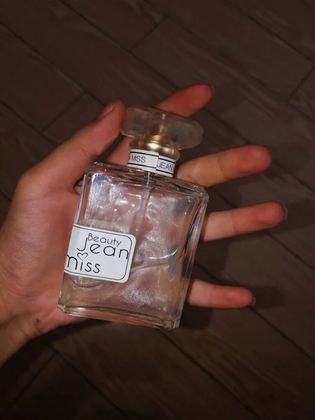 female hand holding bottle of perfume on wooden background