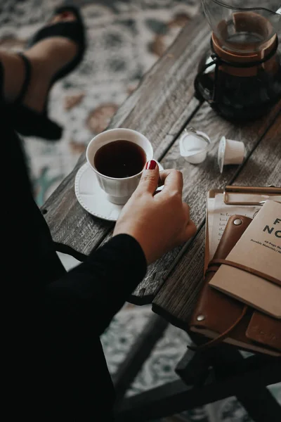 woman's hands with a cup of coffee and a book on a wooden table
