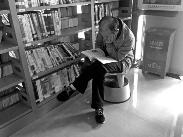 young man in a black and white t-shirt reading a book in the library