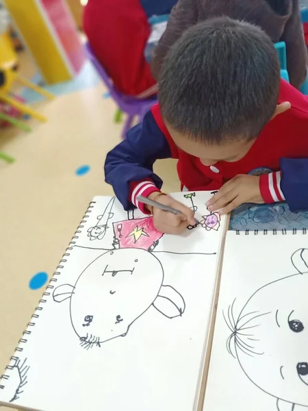 little boy draws a paper with a pencil on the white sheet of a child