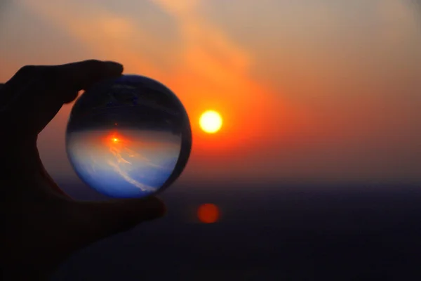 hand holding a glass ball on the background of the sunset.