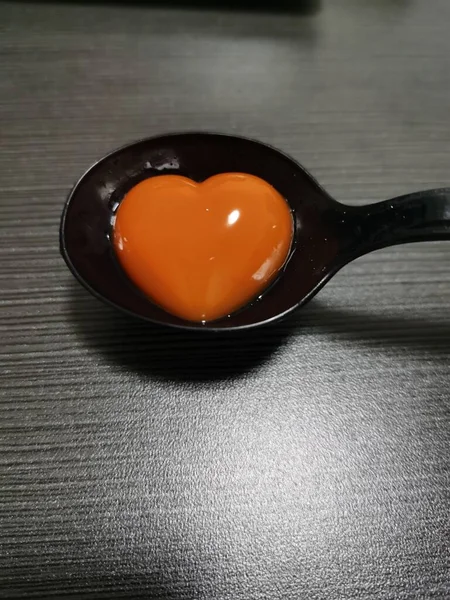 heart shaped egg in a spoon on a black background