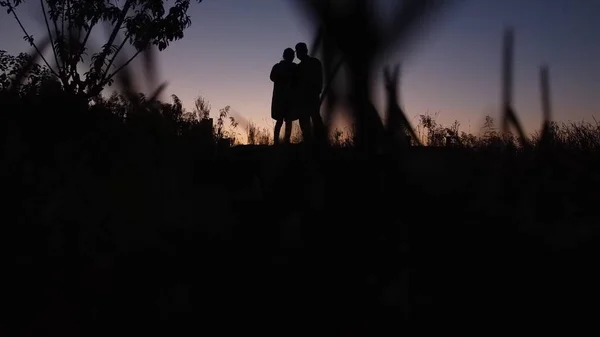 silhouette of a man and a woman in a black dress with a backpack on the background of the sunset