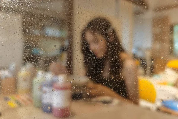 young woman with wet glass and rain drops on the window