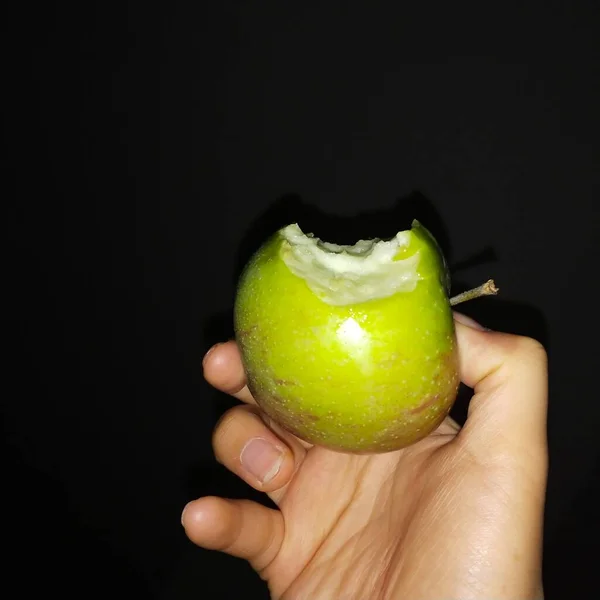 hand holding a green apple on a black background