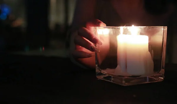 candle in the hands of a woman in a glass
