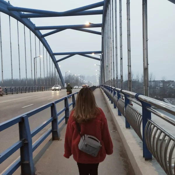 young woman with backpack walking on bridge in city