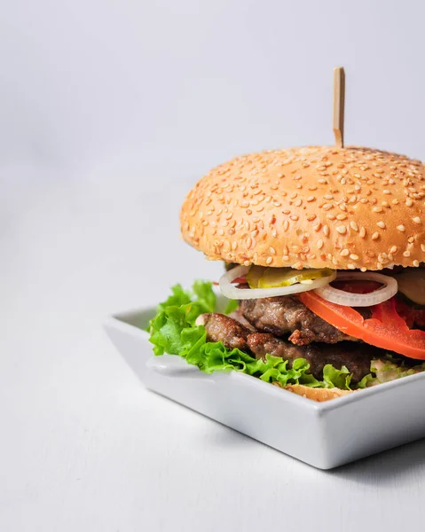 tasty burger with chicken, cheese and tomato, lettuce and salad on white wooden background