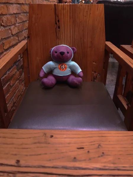 a little bear sits on a bench in a room with a pink background