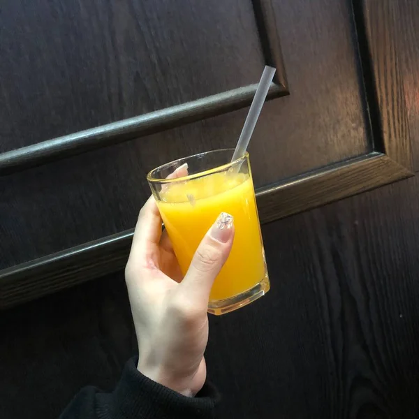 hand holding a glass of orange juice on a wooden table