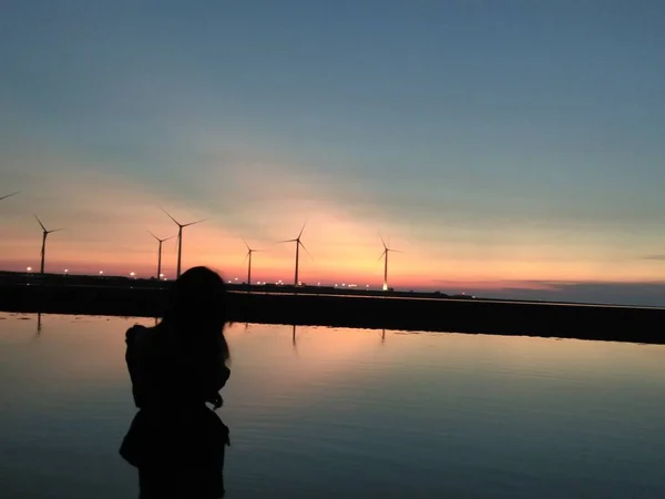 silhouette of a woman with a wind turbine on the background of the sunset