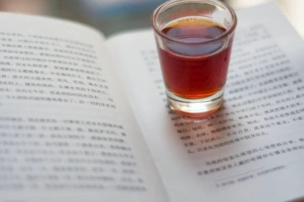 a cup of tea and a book on a background of a glass of wine