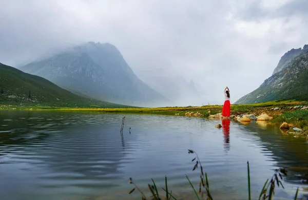 woman in a green jacket sits on a lake in the mountains