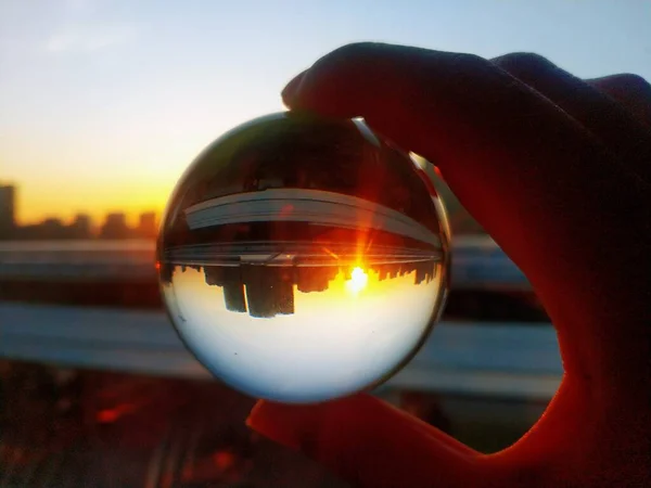 hand holding glass ball with sunset sky background