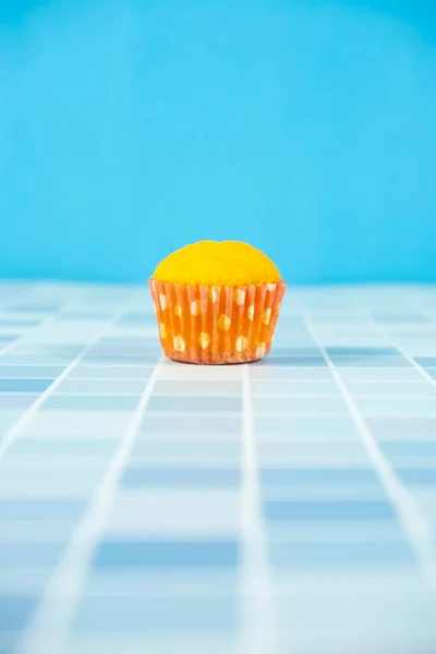 close up of a blue and yellow cupcake on a turquoise background