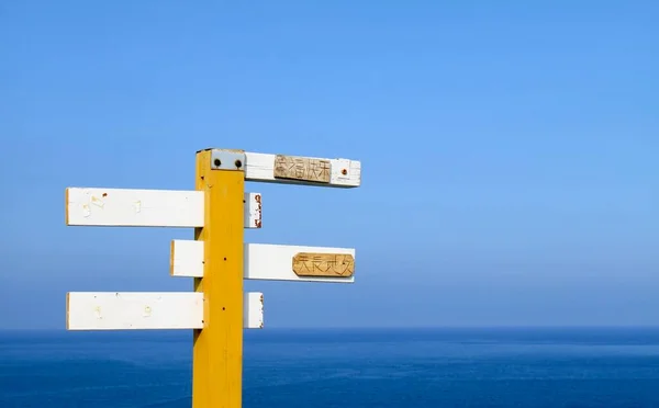 a vertical shot of a wooden signpost with a blue sky