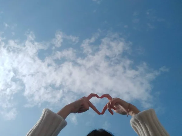 heart shape concept. human hands holding a white cloud on a blue sky background.