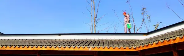 a man in a red t-shirt is standing on a roof of a house