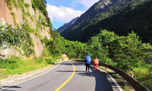 a man and a woman in a green jacket and a backpack on a mountain road in the mountains
