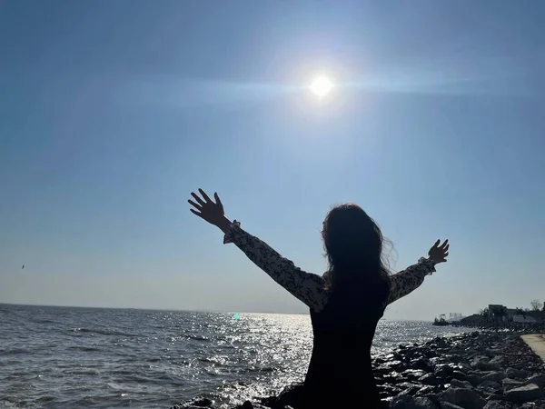 silhouette of a woman with a raised hands on the sea