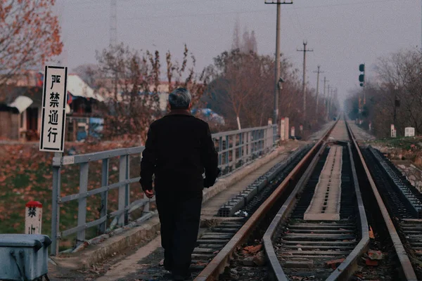 a man in a black jacket and a red hat stands on the railway tracks