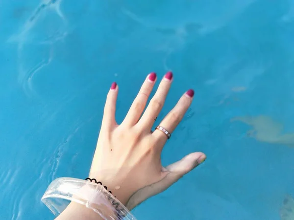 woman's hands with a blue manicure on a background of a pool.