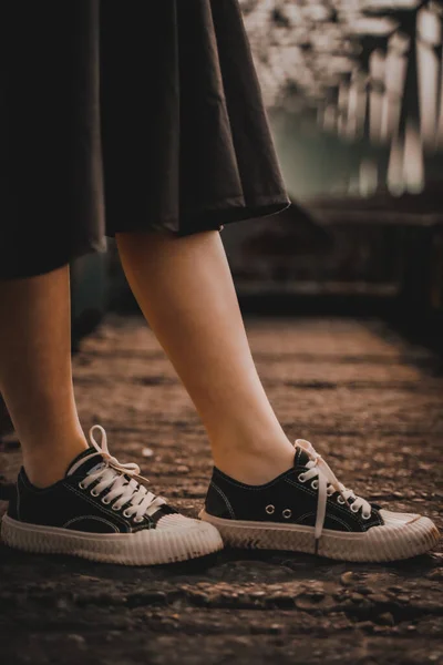 cropped view of woman holding shoes with legs on wooden background