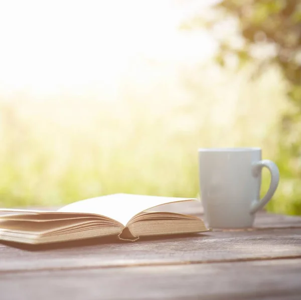open book with coffee cup on wooden table in nature