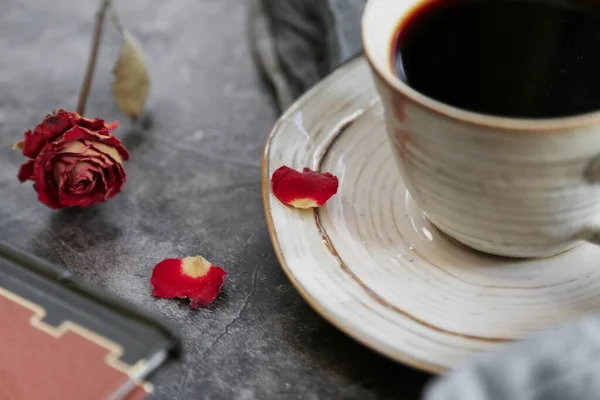 cup of tea with red roses and a book on a wooden background