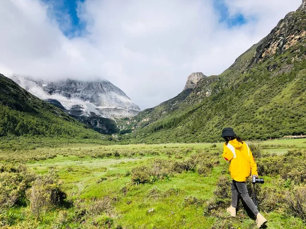 man in a green jacket and a backpack with a mountain in the background