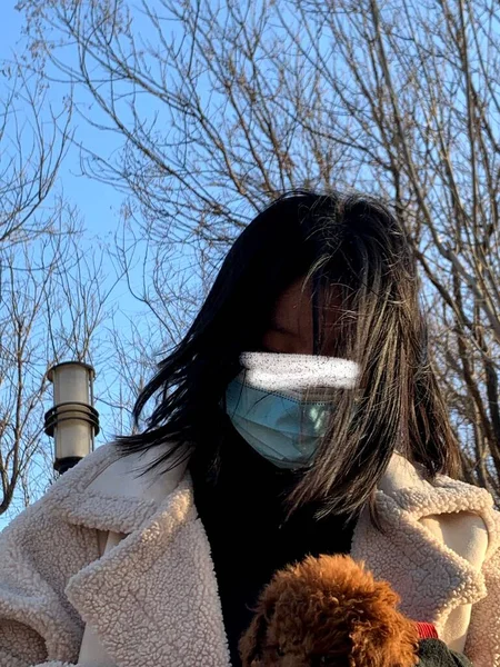 woman in a protective mask and a scarf on a background of a blue sky