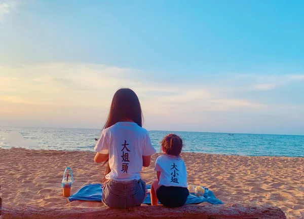 mother and daughter sitting on the beach at sunset